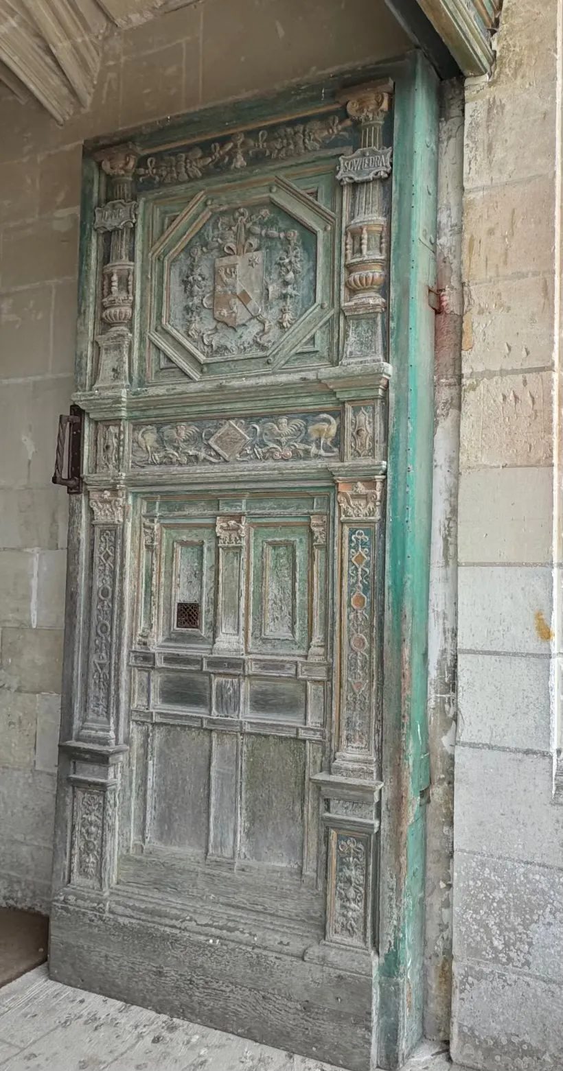 A tall carved wooden door with weathered green paint, set in a stone archway.